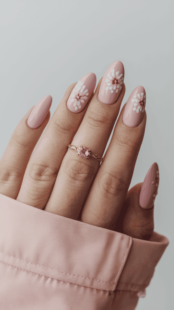 A hand with pink, floral-patterned nail art and a pink gemstone ring on the ring finger; the sleeve of a pink garment is partially visible.