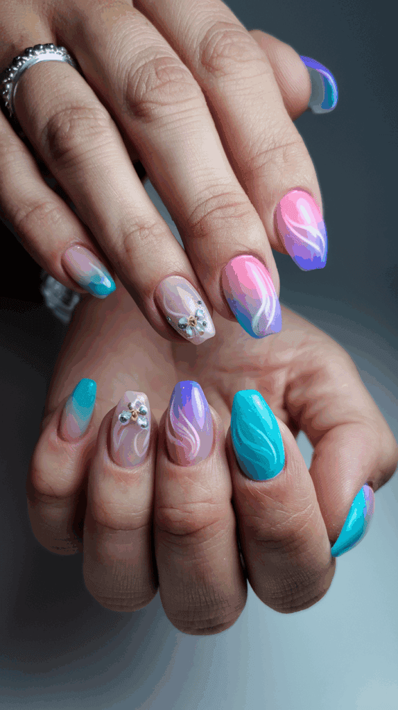 Close-up of hands with stylishly manicured nails featuring gradient pink, purple, and teal colors with white swirl designs and small rhinestone embellishments on some nails.