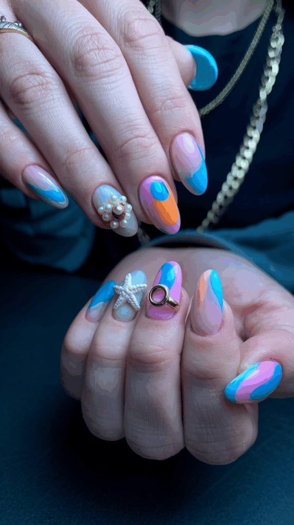 Close-up of hands with colorful, wavy nail art in shades of blue, pink, orange, and white, featuring pearl and starfish embellishments.