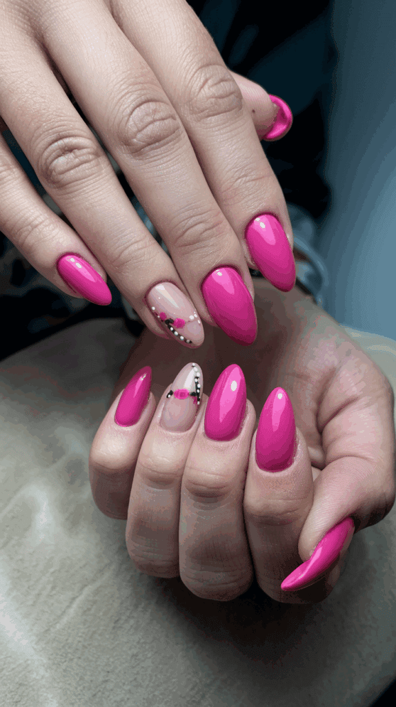 Hands with long, almond-shaped nails painted in glossy pink, with two nails featuring a floral design on a nude background with black and white accents.