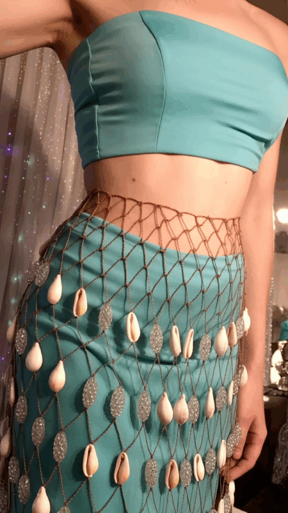 A person wearing a turquoise tube top and matching skirt with a fishnet overlay decorated with shells and beads.